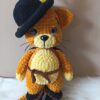 Csizmás Kandúr amigurumi figura, sárgás-narancs zseníliafonálból horgolt, fekete kalappal, sárga tollal, barna övvel és fekete csizmával, zöld szemekkel