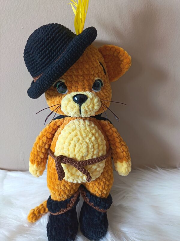 Csizmás Kandúr amigurumi figura, sárgás-narancs zseníliafonálból horgolt, fekete kalappal, sárga tollal, barna övvel és fekete csizmával, zöld szemekkel